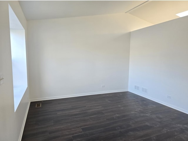 empty room with lofted ceiling, visible vents, dark wood finished floors, and baseboards