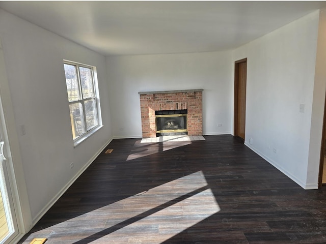 unfurnished living room with a brick fireplace, wood finished floors, and baseboards