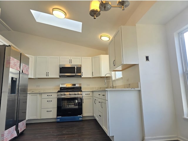 kitchen featuring appliances with stainless steel finishes, vaulted ceiling with skylight, dark wood-style flooring, and white cabinetry