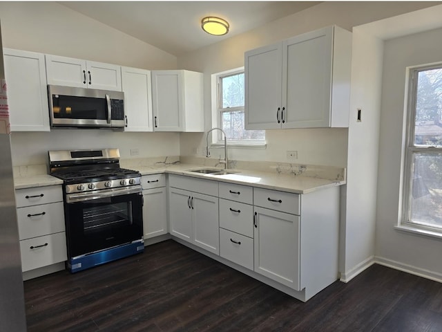 kitchen featuring lofted ceiling, appliances with stainless steel finishes, dark wood-type flooring, white cabinetry, and a sink