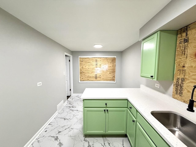 kitchen featuring baseboards, green cabinetry, a sink, light countertops, and marble finish floor