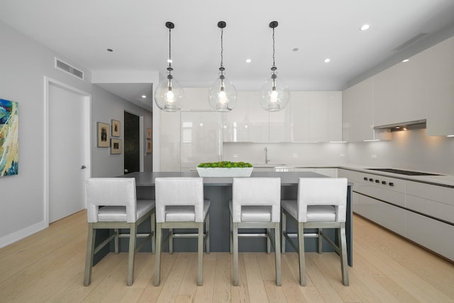 kitchen featuring under cabinet range hood, electric cooktop, a sink, white cabinetry, and visible vents