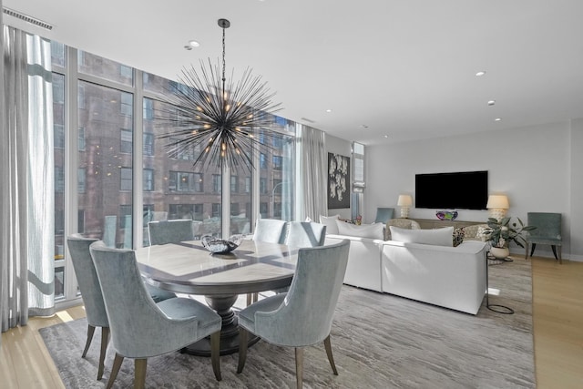 dining space featuring light wood-type flooring, an inviting chandelier, a wall of windows, and recessed lighting