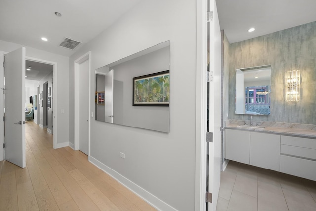 hallway with baseboards, visible vents, light wood-style floors, a sink, and recessed lighting