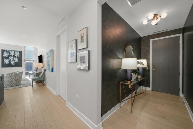 hall featuring light wood-type flooring, baseboards, an accent wall, and visible vents