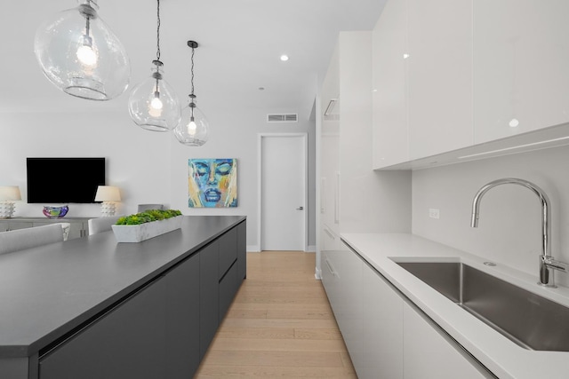 kitchen with visible vents, modern cabinets, light wood-style floors, white cabinetry, and a sink