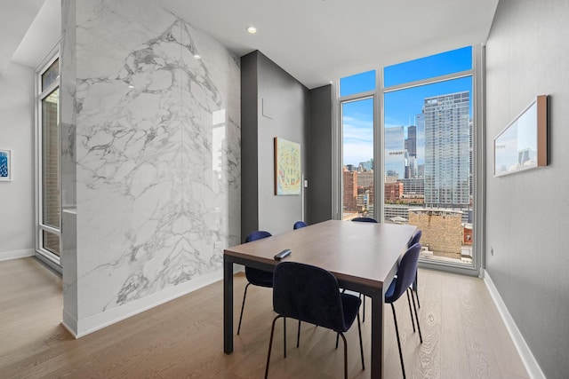 dining room with baseboards, light wood-style flooring, a view of city, floor to ceiling windows, and recessed lighting