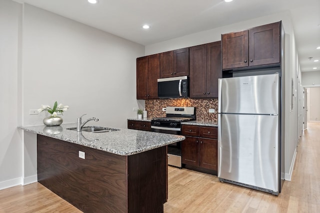 kitchen with light wood-type flooring, a sink, backsplash, appliances with stainless steel finishes, and dark brown cabinets