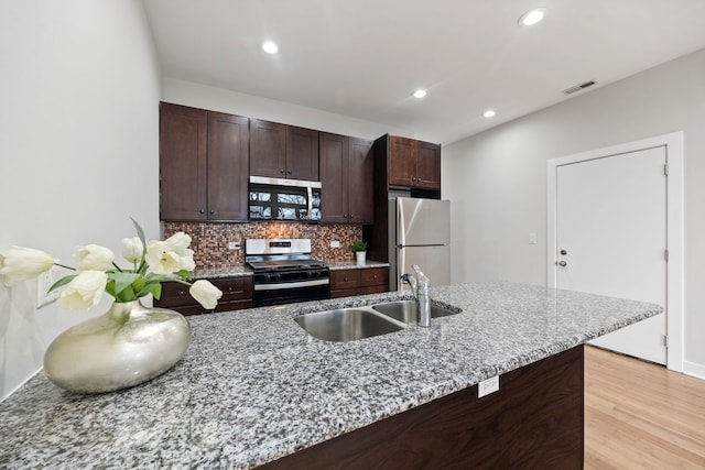 kitchen with a sink, dark brown cabinets, appliances with stainless steel finishes, light wood-type flooring, and backsplash