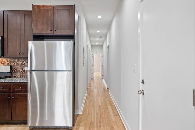 kitchen featuring light wood-style floors, backsplash, dark brown cabinets, and freestanding refrigerator