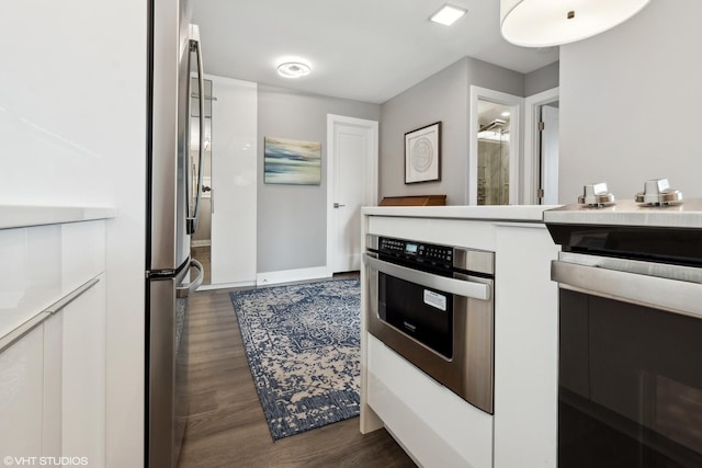 kitchen with stainless steel appliances, light countertops, white cabinetry, and dark wood-style floors