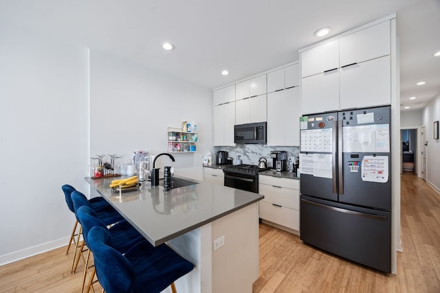 kitchen featuring a breakfast bar, white cabinetry, a sink, and black appliances