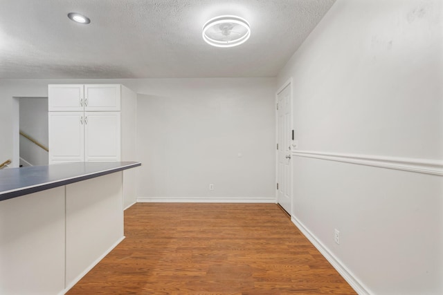 interior space with a textured ceiling, baseboards, and wood finished floors