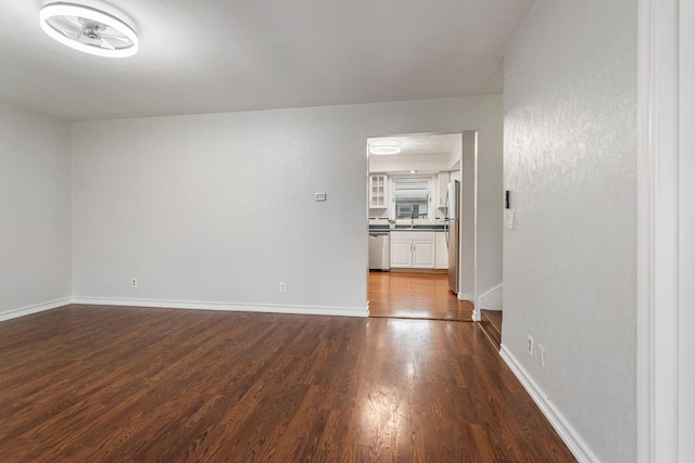 empty room featuring a sink, baseboards, and dark wood-style flooring