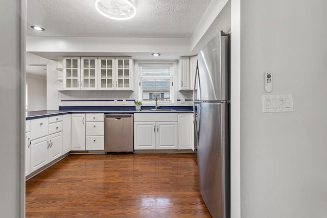 kitchen featuring white cabinets, dark countertops, glass insert cabinets, stainless steel appliances, and a sink