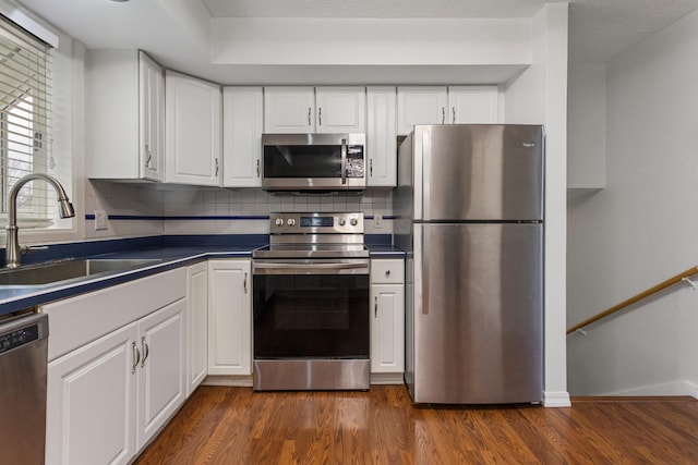 kitchen with white cabinets, dark countertops, dark wood-style floors, stainless steel appliances, and a sink