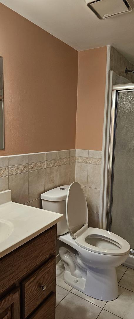 bathroom featuring toilet, vanity, tile walls, a shower stall, and tile patterned floors