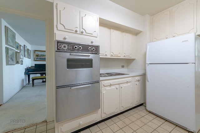 kitchen with light tile patterned floors, electric stovetop, white cabinets, light countertops, and freestanding refrigerator