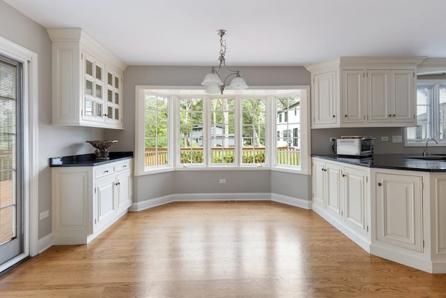 kitchen with white cabinetry, baseboards, light wood-type flooring, dark countertops, and glass insert cabinets