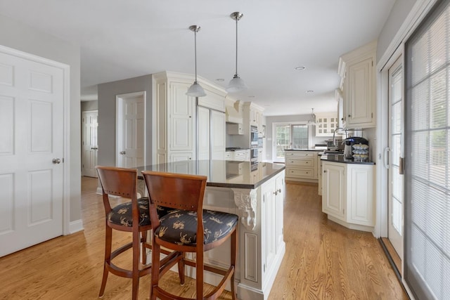 kitchen with dark countertops, a kitchen island, light wood-style flooring, and a kitchen breakfast bar