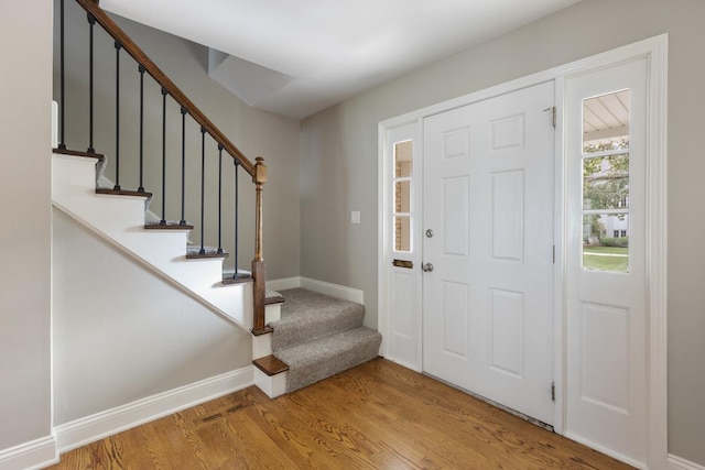 foyer entrance with stairs, wood finished floors, and baseboards