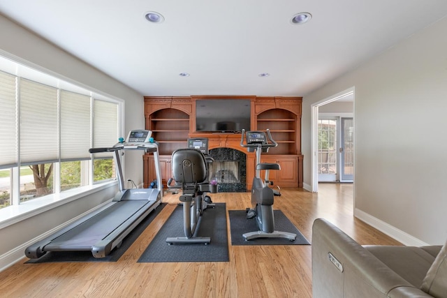 exercise room featuring a high end fireplace, light wood-style flooring, baseboards, and recessed lighting