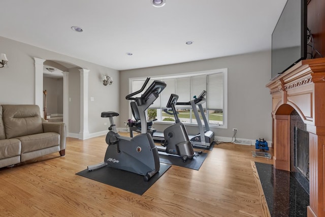 workout room with arched walkways, wood finished floors, a high end fireplace, baseboards, and ornate columns