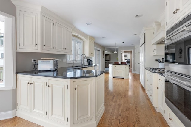 kitchen featuring a peninsula, a sink, white cabinetry, light wood-style floors, and dark countertops