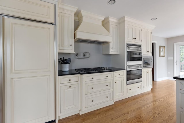 kitchen with stainless steel appliances, premium range hood, light wood-type flooring, and dark countertops