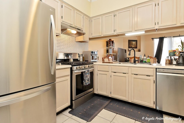 kitchen with stainless steel appliances, light countertops, a sink, under cabinet range hood, and tile patterned floors