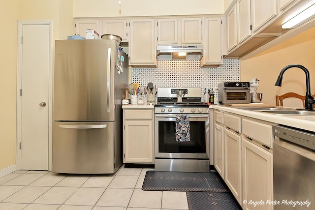 kitchen featuring light tile patterned floors, stainless steel appliances, light countertops, under cabinet range hood, and a sink