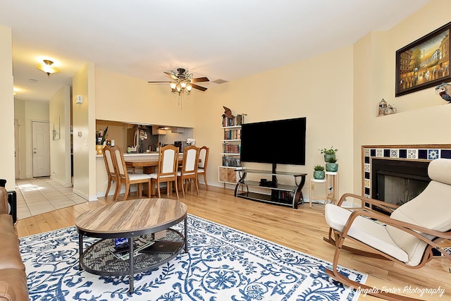 living area with a tile fireplace, ceiling fan, baseboards, and wood finished floors