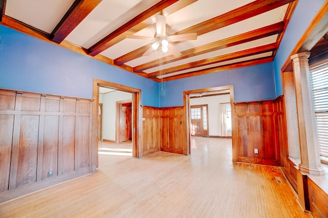 unfurnished room featuring wood finished floors, a ceiling fan, wainscoting, beamed ceiling, and ornate columns