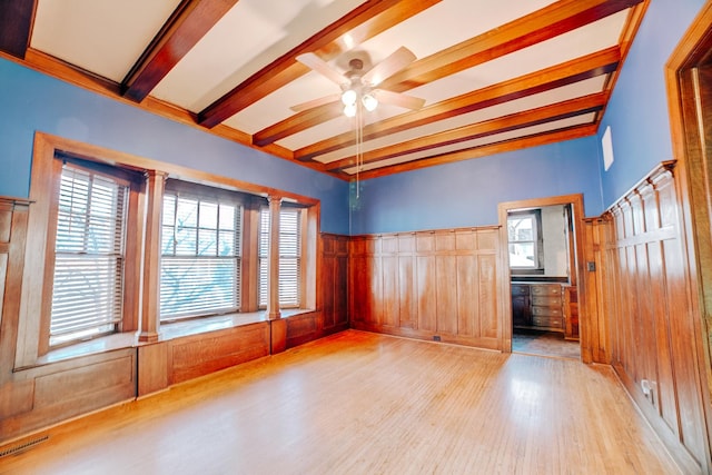 empty room featuring ceiling fan, beamed ceiling, wood finished floors, and visible vents