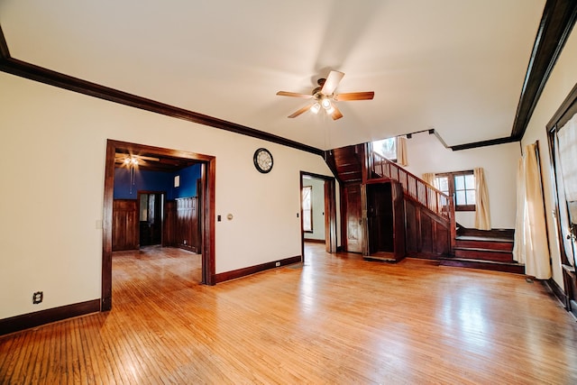 unfurnished living room with baseboards, a ceiling fan, light wood-style flooring, stairway, and crown molding