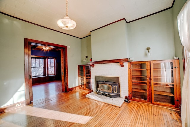 unfurnished living room featuring a wood stove, ornamental molding, hardwood / wood-style floors, and baseboards