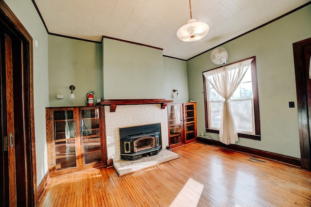 living room featuring baseboards, visible vents, wood-type flooring, a wood stove, and crown molding