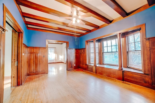 spare room with a healthy amount of sunlight, a ceiling fan, beamed ceiling, and wood finished floors