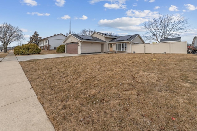 single story home with driveway, solar panels, an attached garage, fence, and a front yard