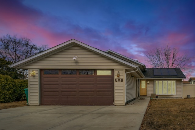 ranch-style house featuring driveway, an attached garage, and roof mounted solar panels