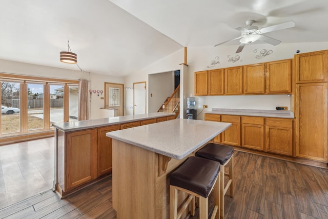 kitchen featuring lofted ceiling, a peninsula, light countertops, brown cabinetry, and dark wood finished floors