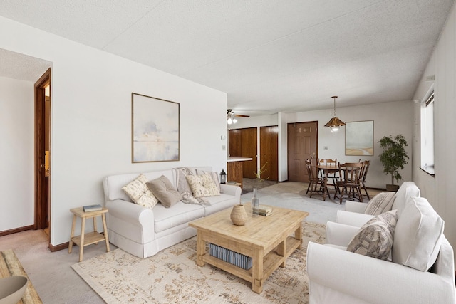 living room featuring baseboards, light colored carpet, ceiling fan, and a textured ceiling