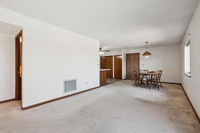 unfurnished dining area featuring visible vents, a ceiling fan, a textured ceiling, baseboards, and light colored carpet