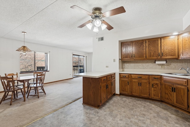 kitchen with visible vents, brown cabinets, a sink, a peninsula, and light countertops