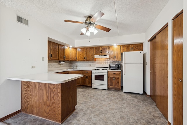 kitchen featuring visible vents, brown cabinets, under cabinet range hood, white appliances, and a peninsula