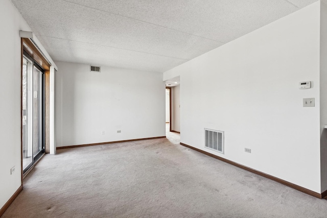 carpeted empty room featuring visible vents, a textured ceiling, and baseboards