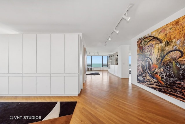 corridor featuring rail lighting, floor to ceiling windows, and light wood finished floors