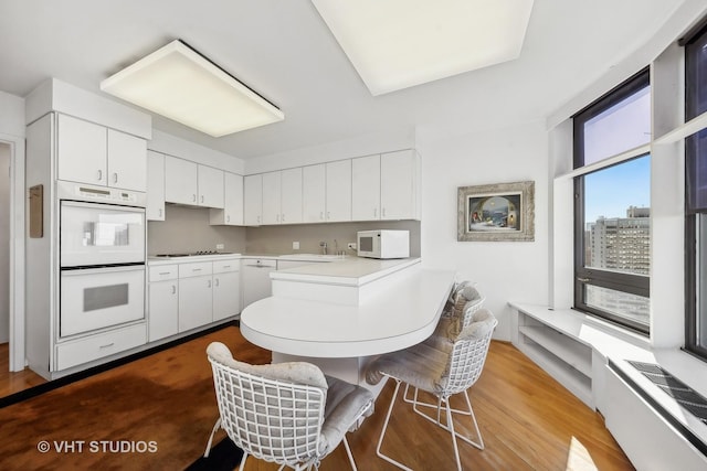 kitchen featuring a breakfast bar area, light countertops, white cabinetry, white appliances, and a peninsula