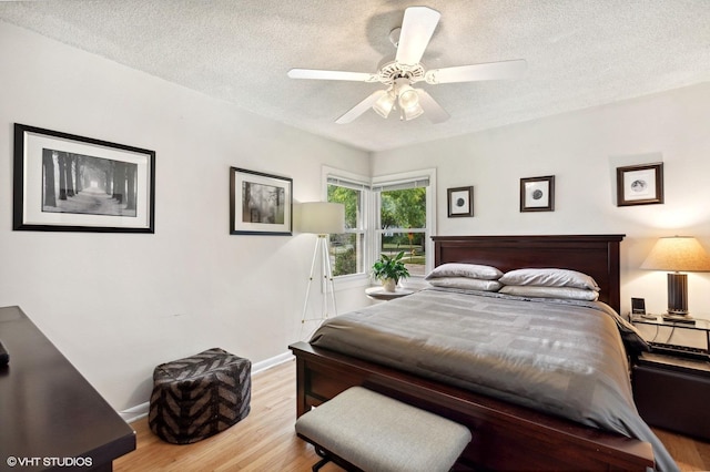 bedroom with a ceiling fan, wood finished floors, baseboards, and a textured ceiling