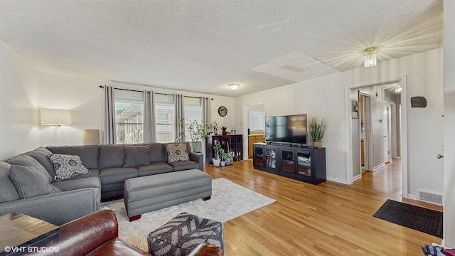 living area featuring light wood finished floors, visible vents, a textured ceiling, and baseboards